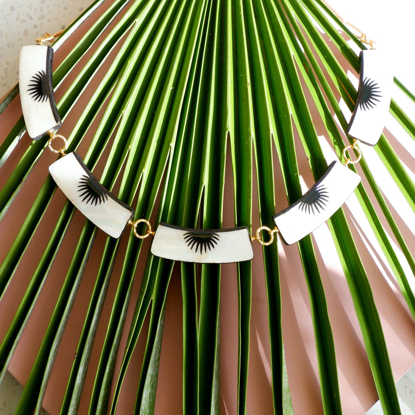 graphic black & white palm design mother of pearl necklace with 5 panels, on golden long-link chain on palm leaf