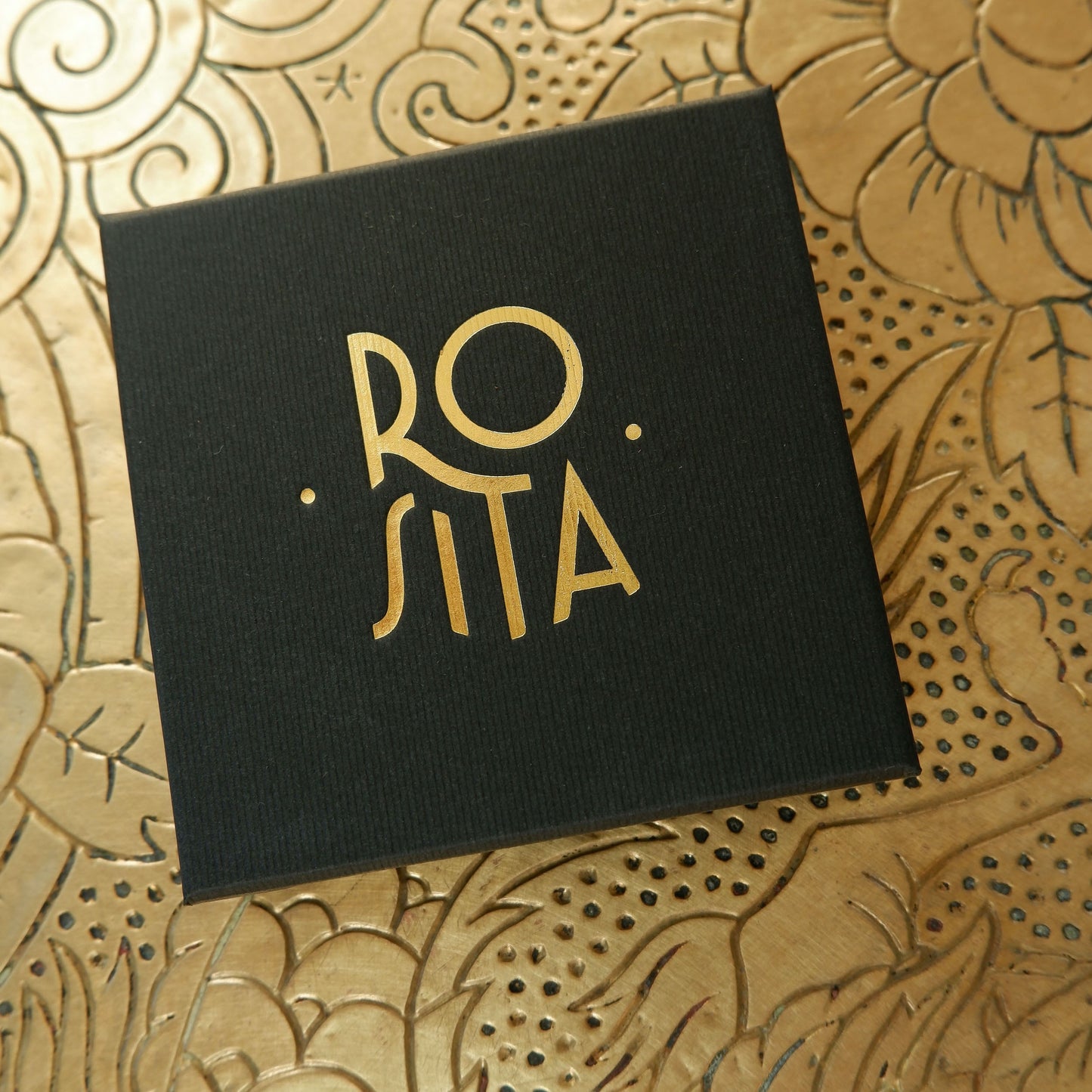 Black finely ribbed cardboard jewellery box, with ROSITA logo branding in Gold foil, on gold patterned background
