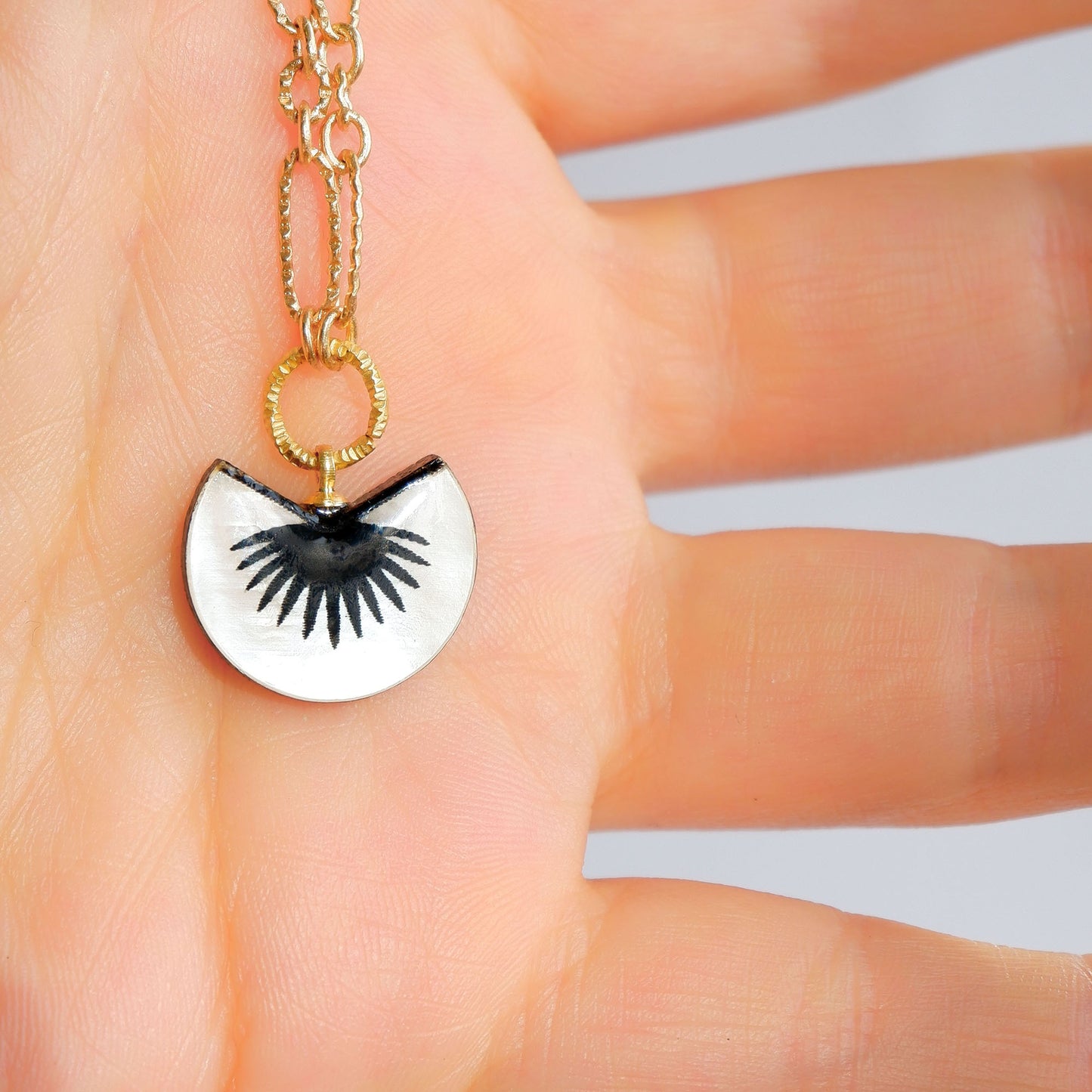 Black & mother of pearl graphic palm design pendant of golden chain, on a hand