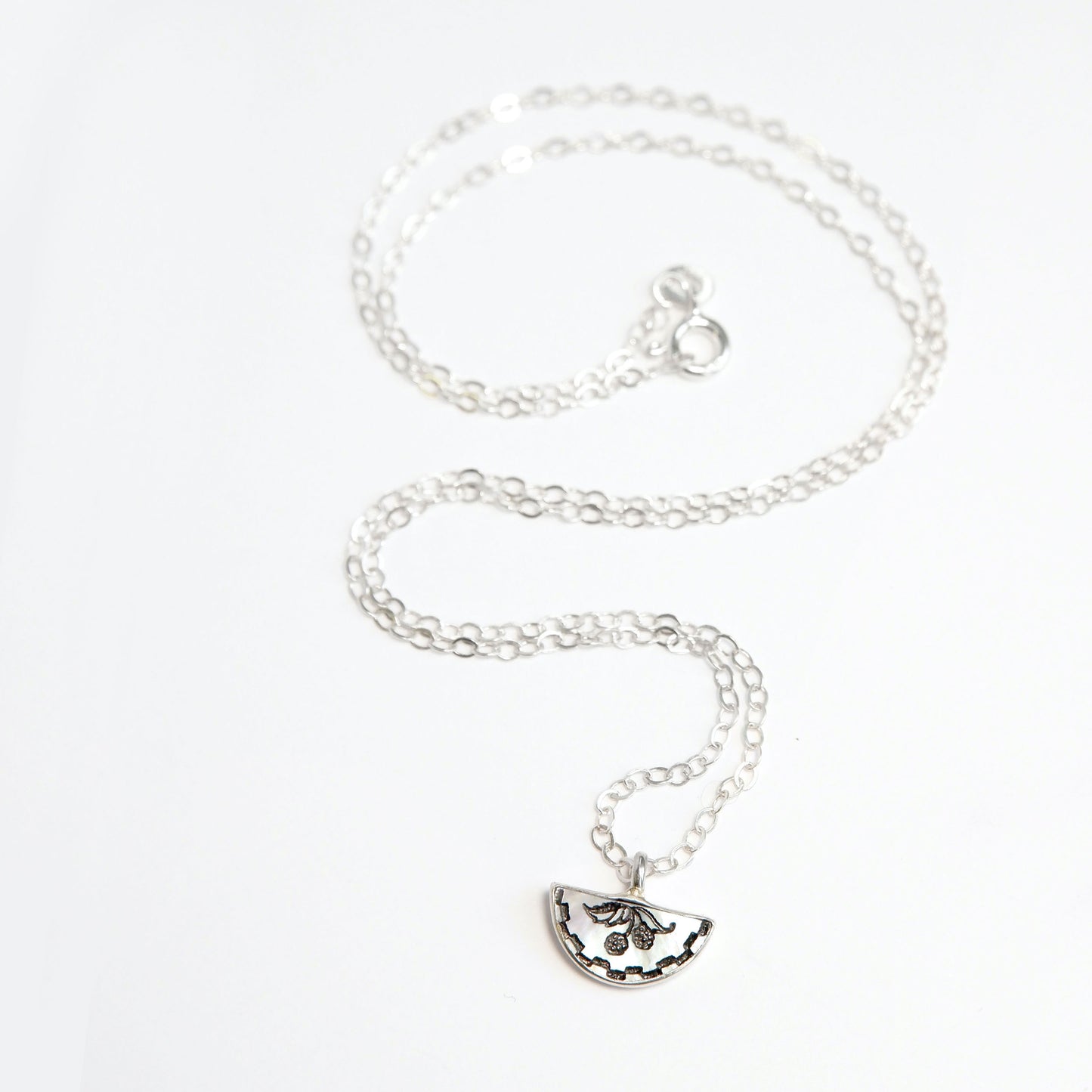 little mother of pearl half moon pendant, engraved with blackberry design, with checquerboard border, on fine sterling silver chain.