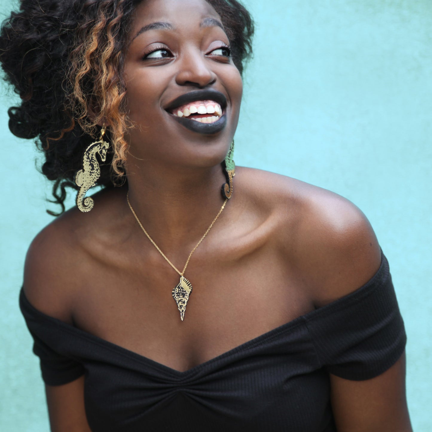 model wearing black & gold leather seahorse earrings & twister shell epndant, pale blue background