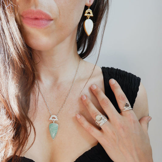structural open-work ring in a bamboo style, featuring a faceted round golden brown Montana Agate gemstone in a scalloped setting. Sterling Silver. shown on model for scale, with another sterling silver bamboo style ring with pointed gemstone, arched bamboo earring & pendant necklace with pear shaped gemstone drops charms.