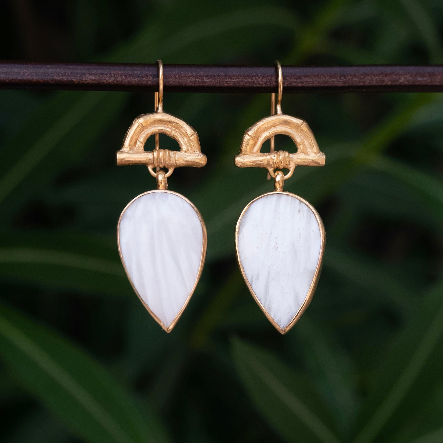 Gold Vermeil hook earrings featuring bamboo sunrise arch design, with pointed gemstone drop pendants in white scolecite, against botanical backdrop
