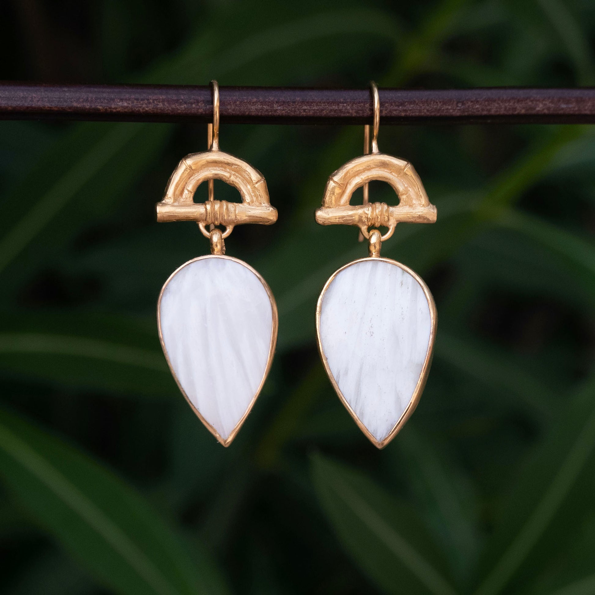 Gold Vermeil hook earrings featuring bamboo sunrise arch design, with pointed gemstone drop pendants in white scolecite, against botanical backdrop
