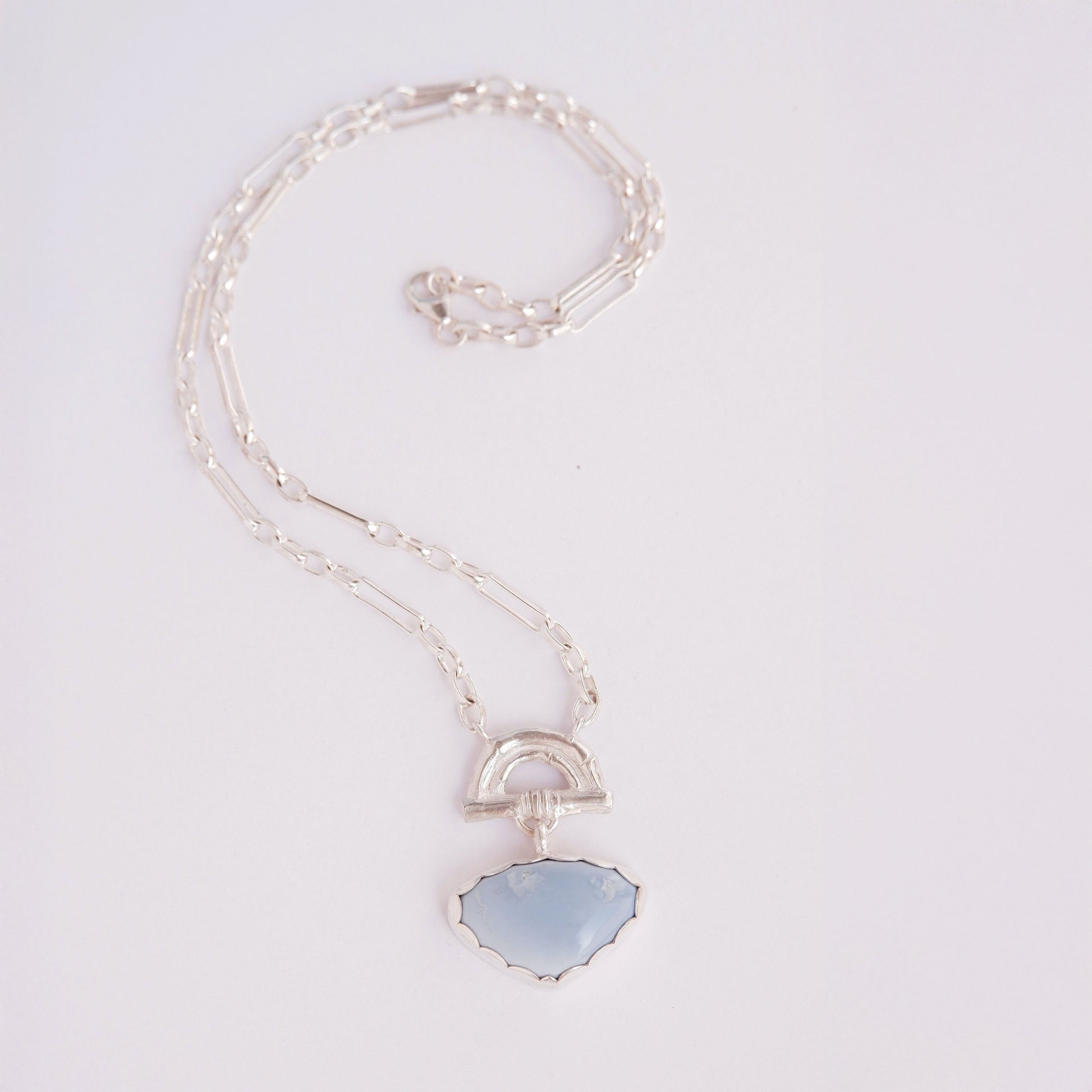Pendant with  heart-shaped pale Blue Opal Gemstone hanging from silver Bamboo Arch, on fine silver chain. white background