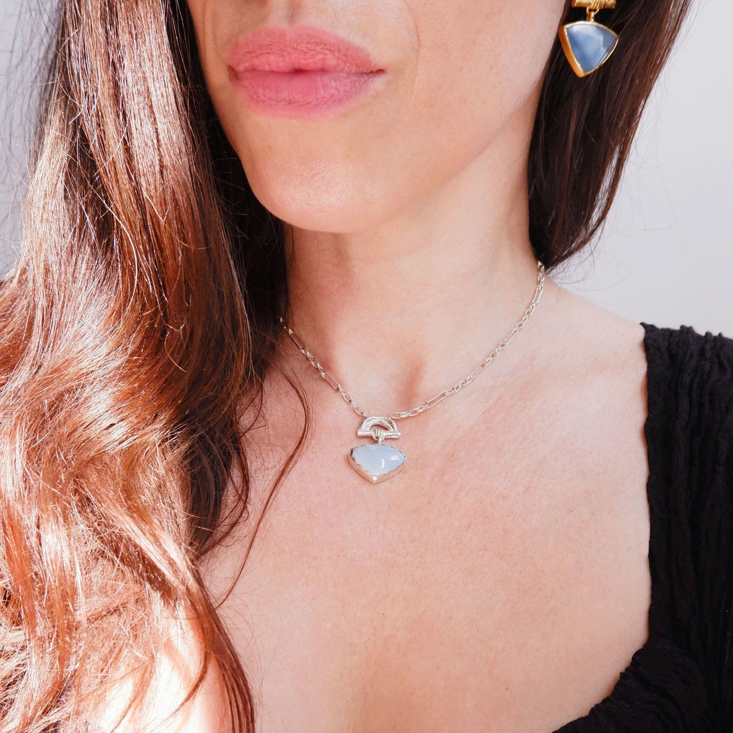 Pendant with  heart-shaped pale Blue Opal Gemstone hanging from silver Bamboo Arch, on fine silver chain. white background. Shown on model, with matching earrings in sky blue opal and gold vermeil.