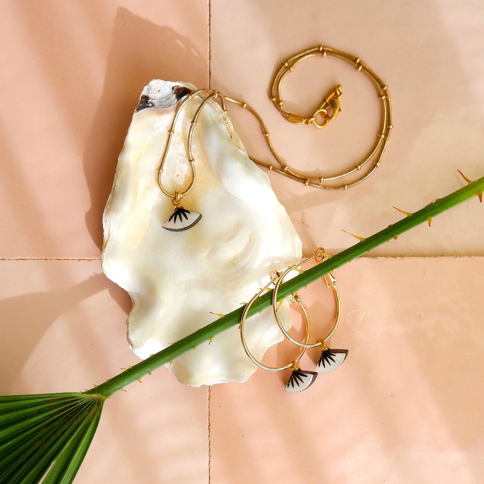 tiny black & mother of pearl graphic pendant on golden beaded snake chain & hoop earrings on oyster shell with palm leaf