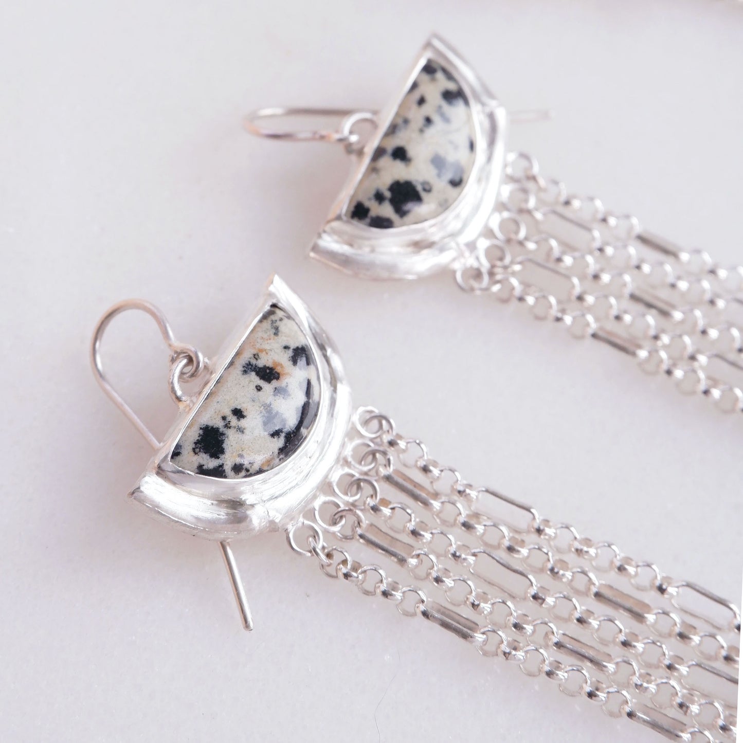 dramatic long chain fringe chandelier tassel earrings with half moon shaped semi precious speckled dalmatian jasper gemstones,  cupped by solid silver bamboo hammock, with simple silver wire hooks. close up cropped shot
