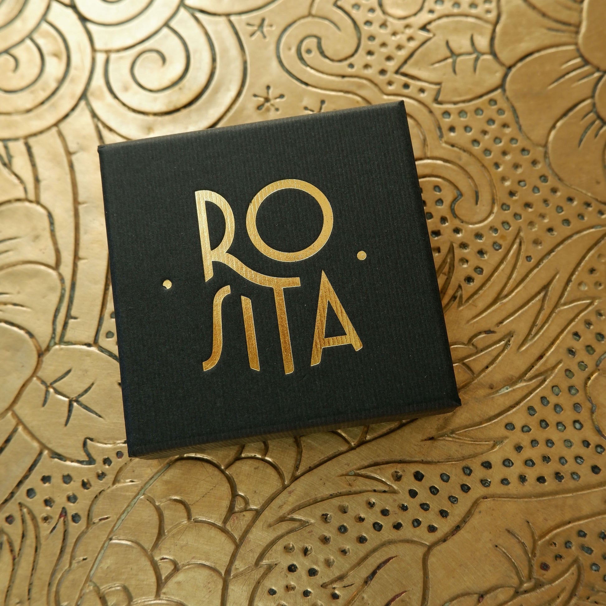 Black finely ribbed cardboard jewellery box, with ROSITA  logo branding in Gold foil, on gold patterned background