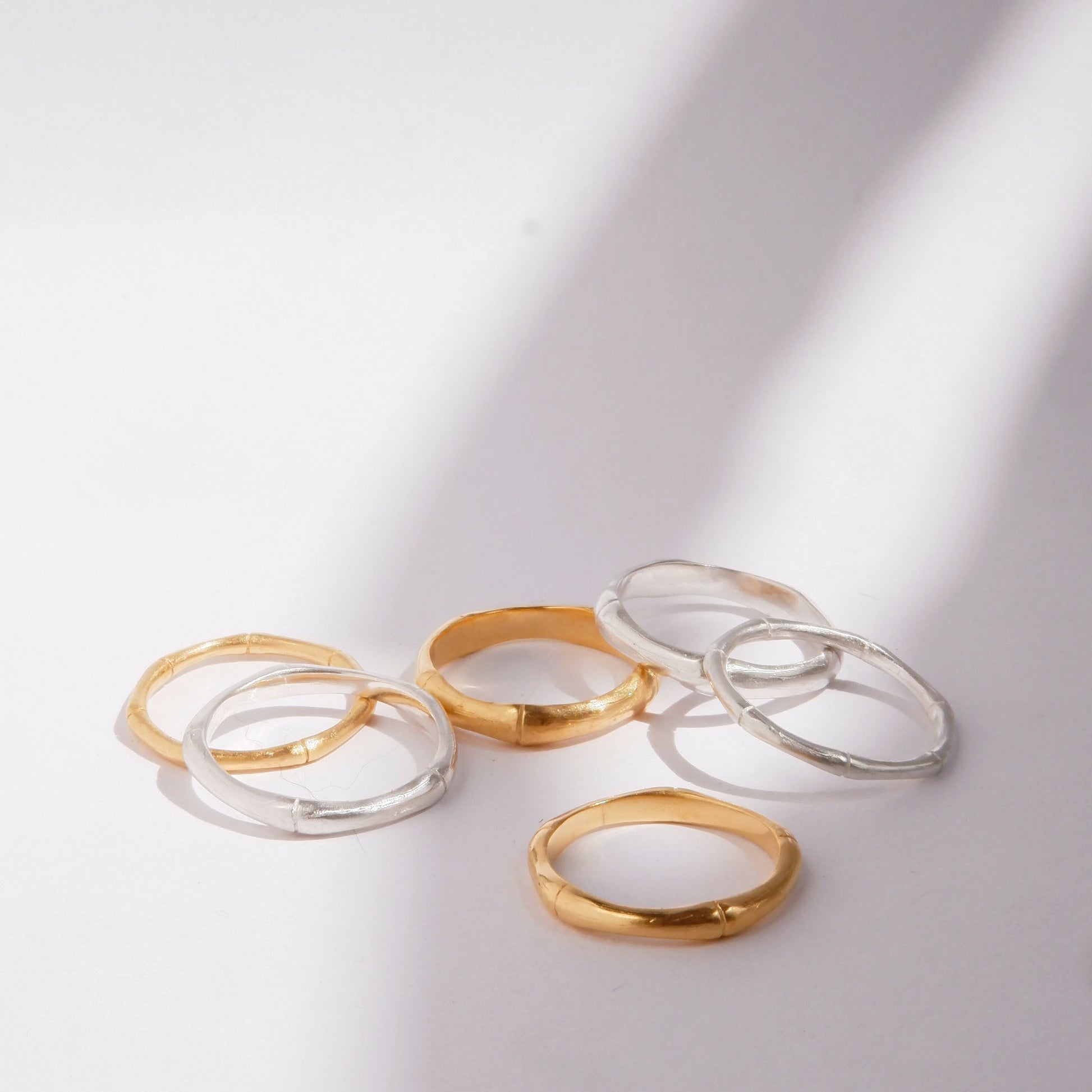 A pile of  bamboo style stacking rings, in three thicknesses in Sterling Silver & Gold Vermeil, white background