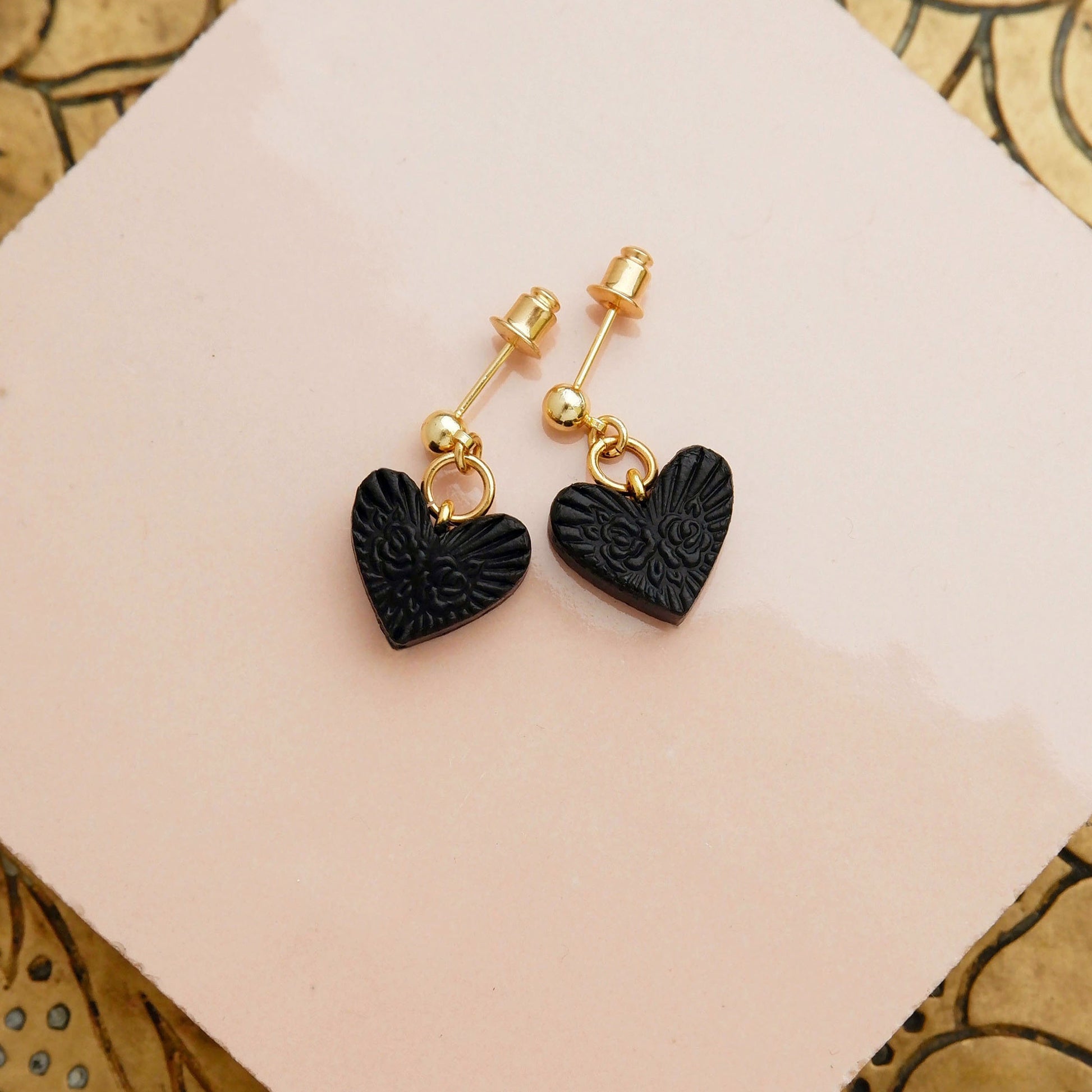 Gold ball stud earrings, with small black, embossed leather heart pendants.