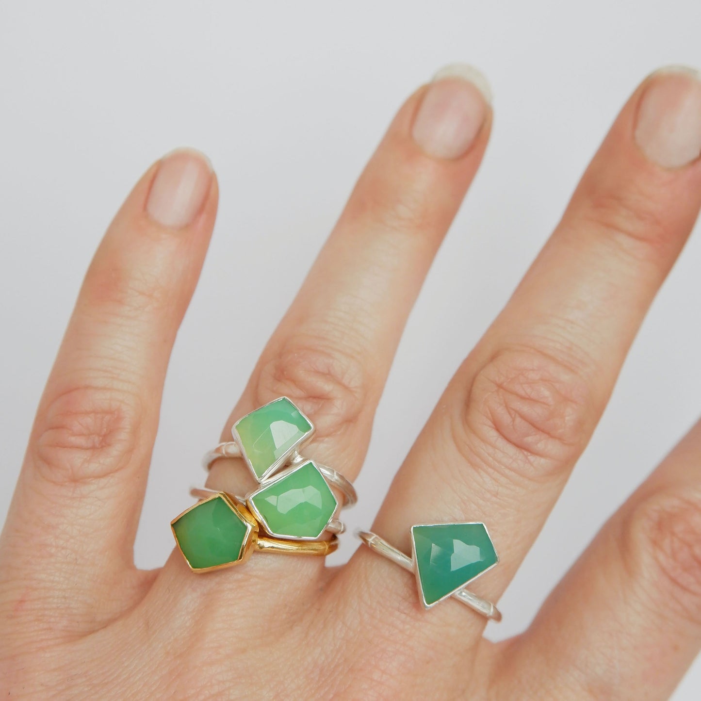 a stack of Sterling Silver and gold vermeil bamboo style rings with irregular angular geometric Chrysoprase gem stones in different shades of green,  on a hand, against a white background