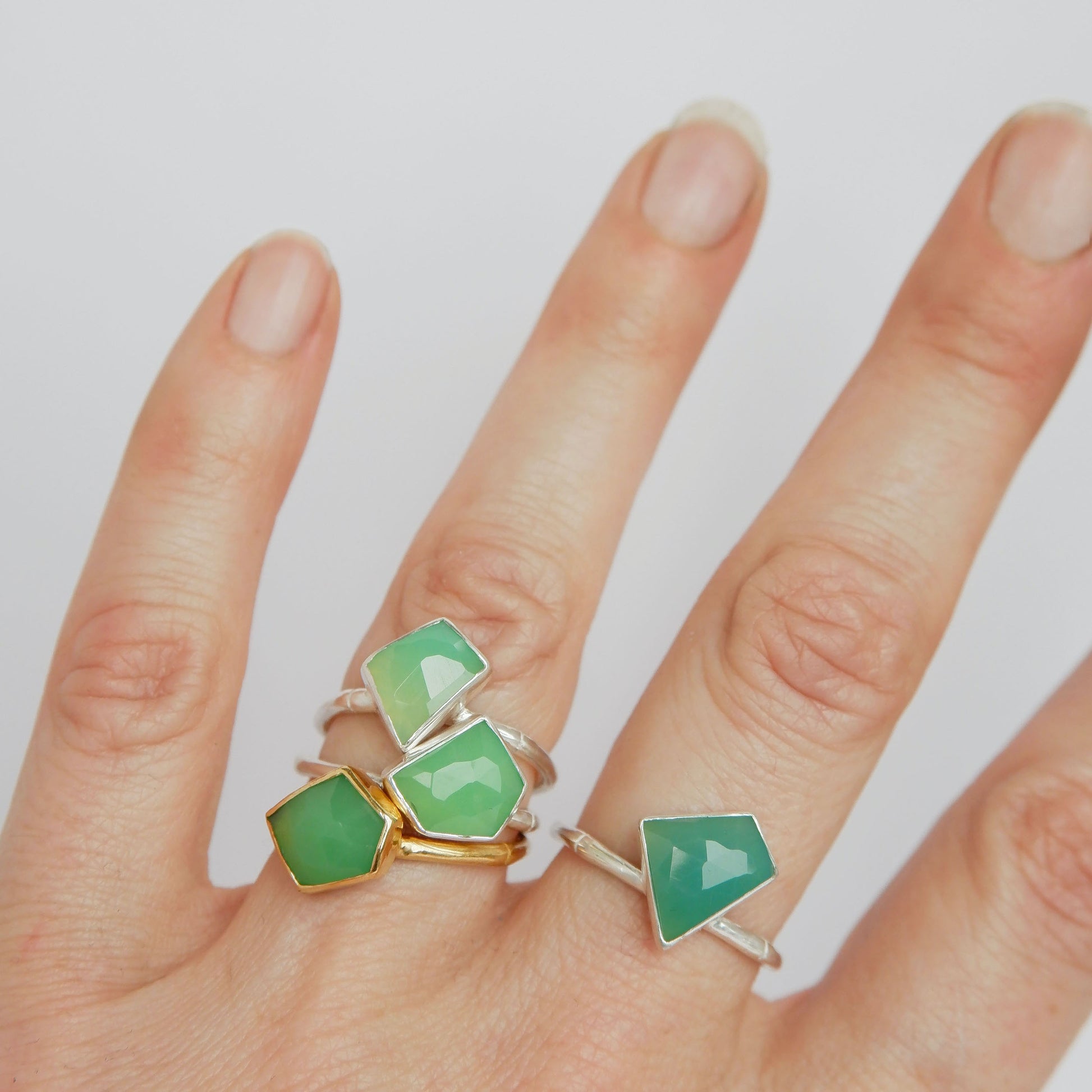 a stack of Sterling Silver and gold vermeil bamboo style rings with irregular angular geometric Chrysoprase gem stones in different shades of green,  on a hand, against a white background