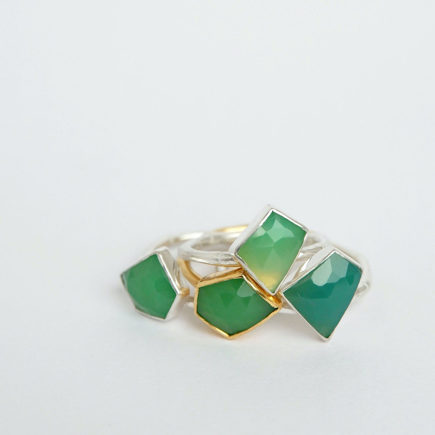 a stack of Sterling Silver and gold vermeil bamboo style rings with irregular angular geometric Chrysoprase gem stones in different shades of green,  against a white background