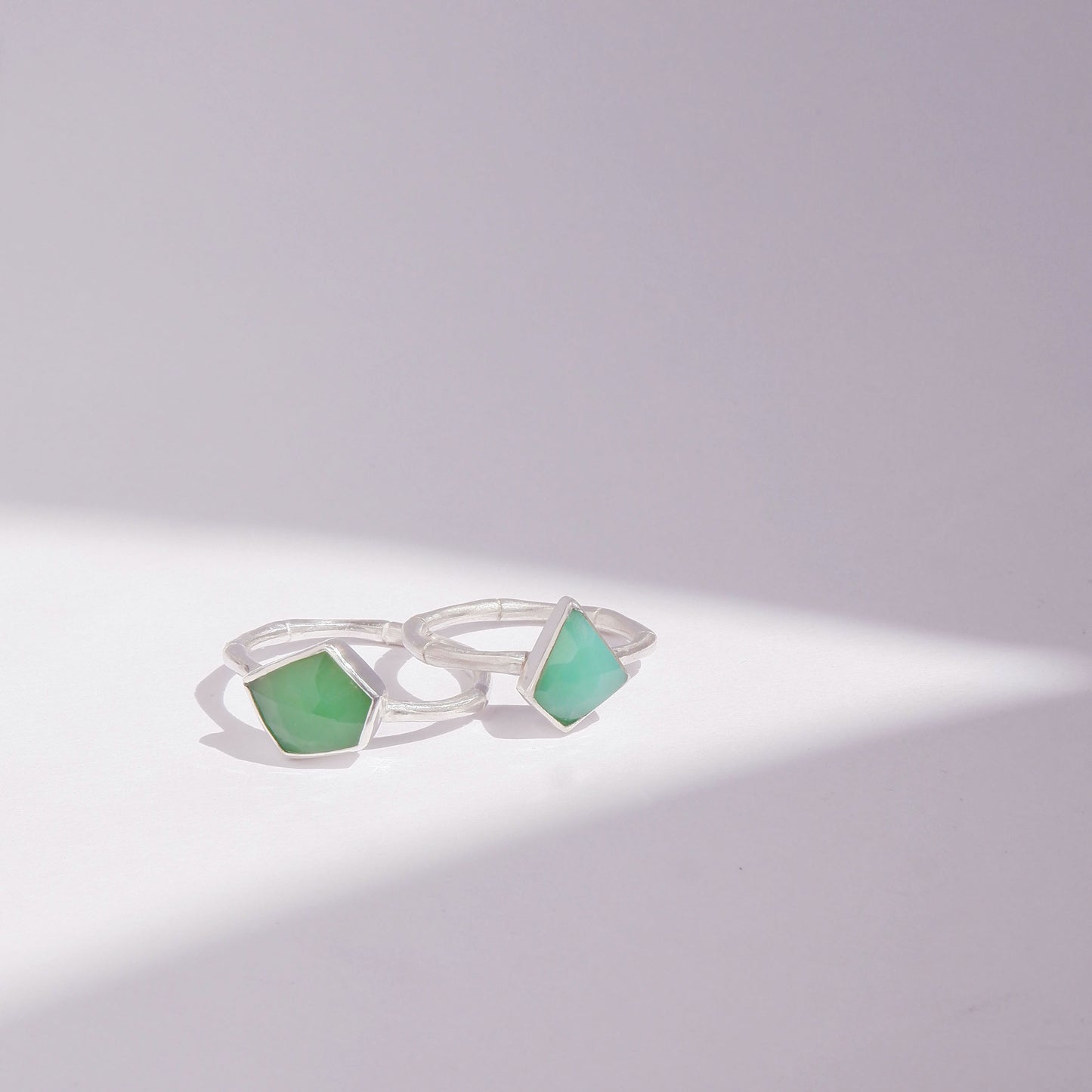 a pair of Sterling Silver bamboo style rings with irregular angular geometric Chrysoprase gem stones in different shades of green, against a white background