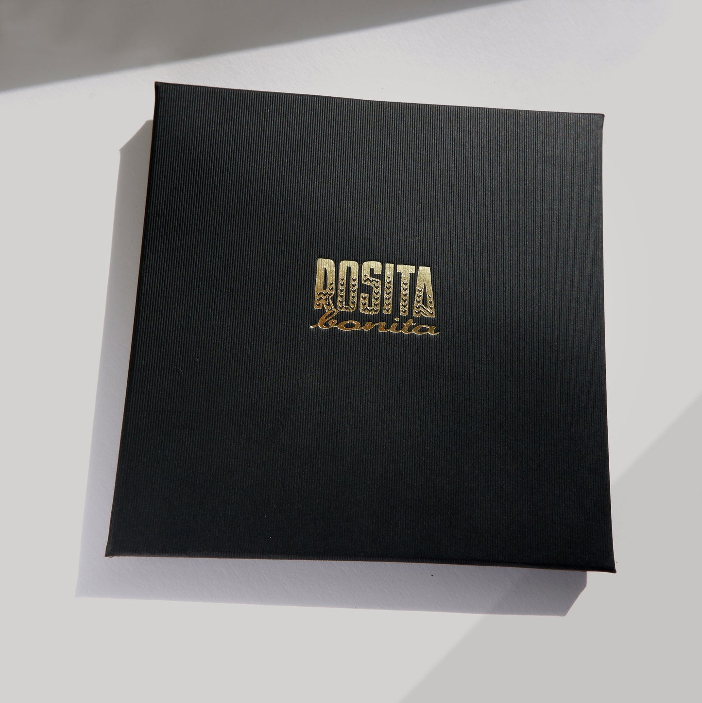 Black pinstripe cardboard box with Rosita Bonita logo in gold