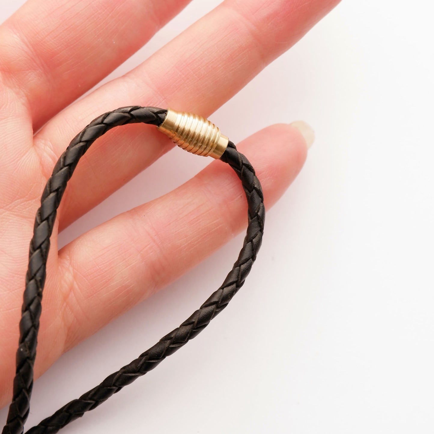 black braided leather bolo cord, with brass magnetic clasp, closed, with hand