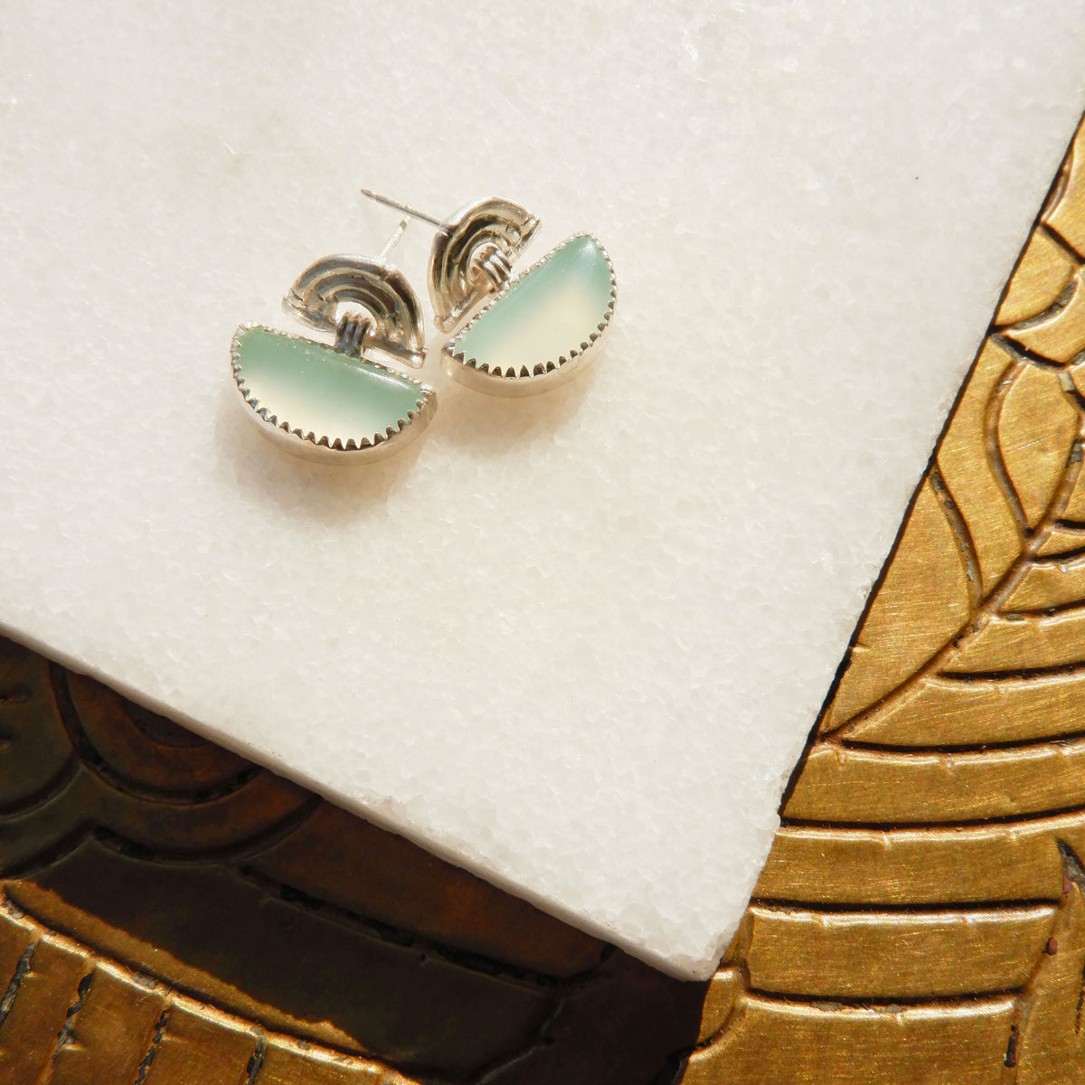 small stud earrings in sterling silver, featuring triple arches of bamboo, hung with a half moon shaped Carnelian gemstone, set with silver teeth, on white marble background
