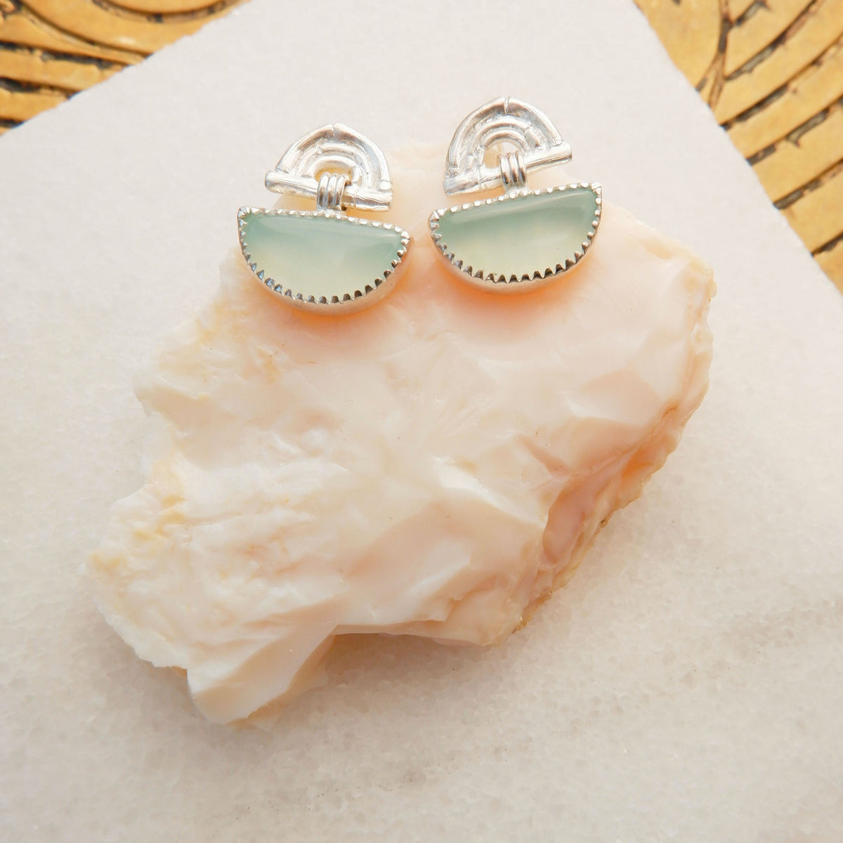 small stud earrings in sterling silver, featuring triple arches of bamboo, hung with a half moon shaped Carnelian gemstone, set with silver teeth., on rough pink stone background
