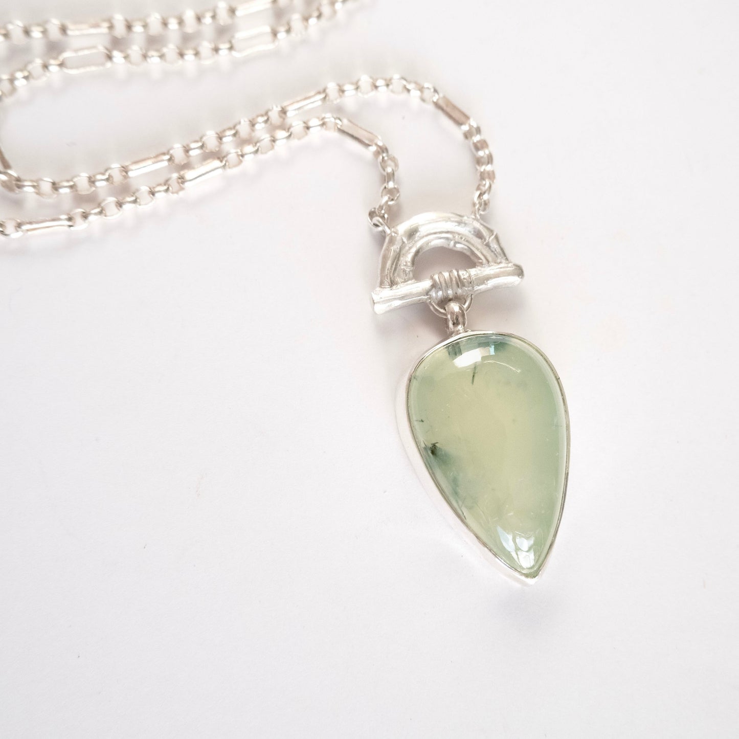 Pendant with  Pear-shaped pale green Prehnite Gemstone hanging from silver Bamboo Arch, on fine silver chain. white background