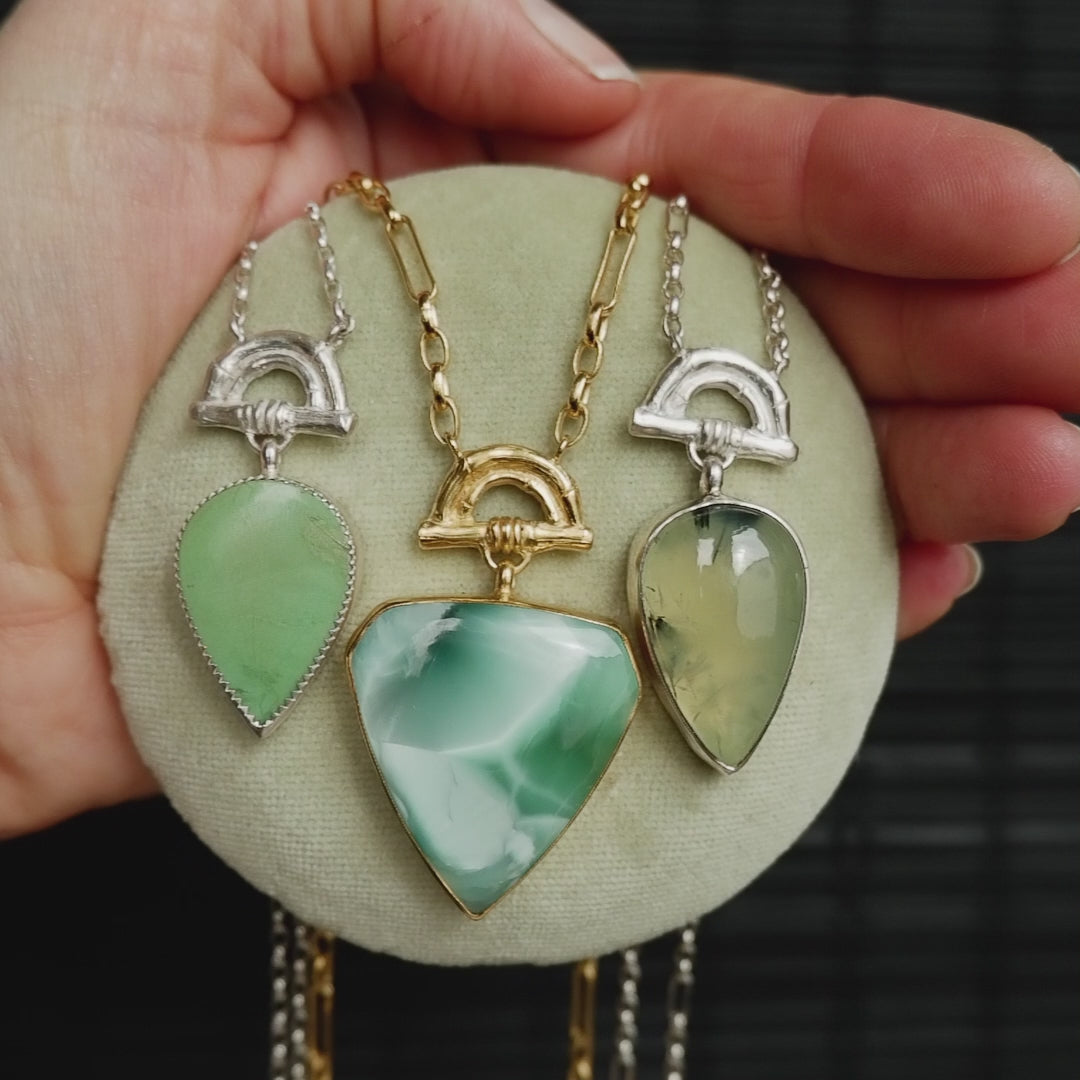 video showing 3 pendants with green turquoise, hemimorphite & Prehnite gemstones hanging from Gold & silver Bamboo Arches on Gold & silver chain.  shown on pale green velvet