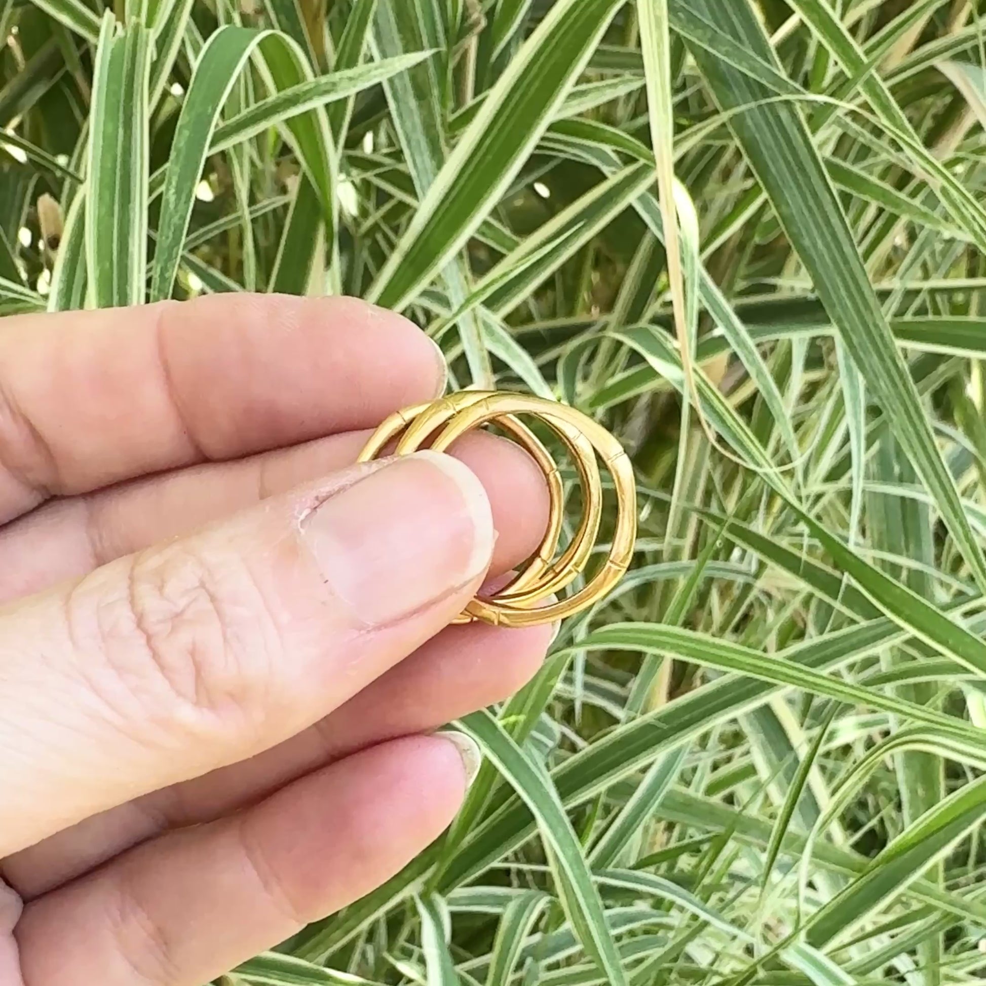 a video of a hand holding bamboo style stacking rings, in three thicknesses in  Gold Vermeil, against bamboo leaf background