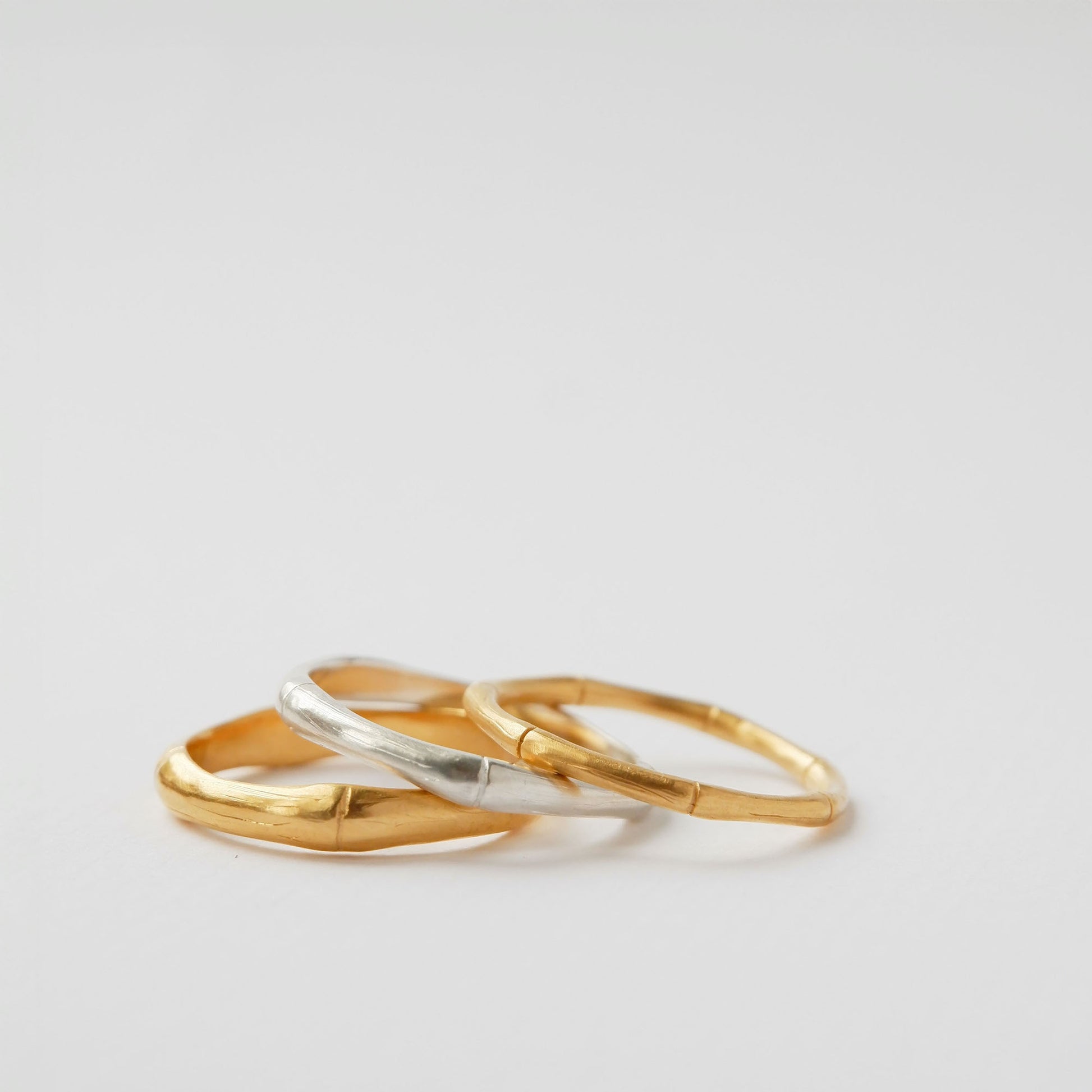 A pile of three bamboo style stacking rings, in three thicknesses in Sterling Silver & Gold Vermeil, white background