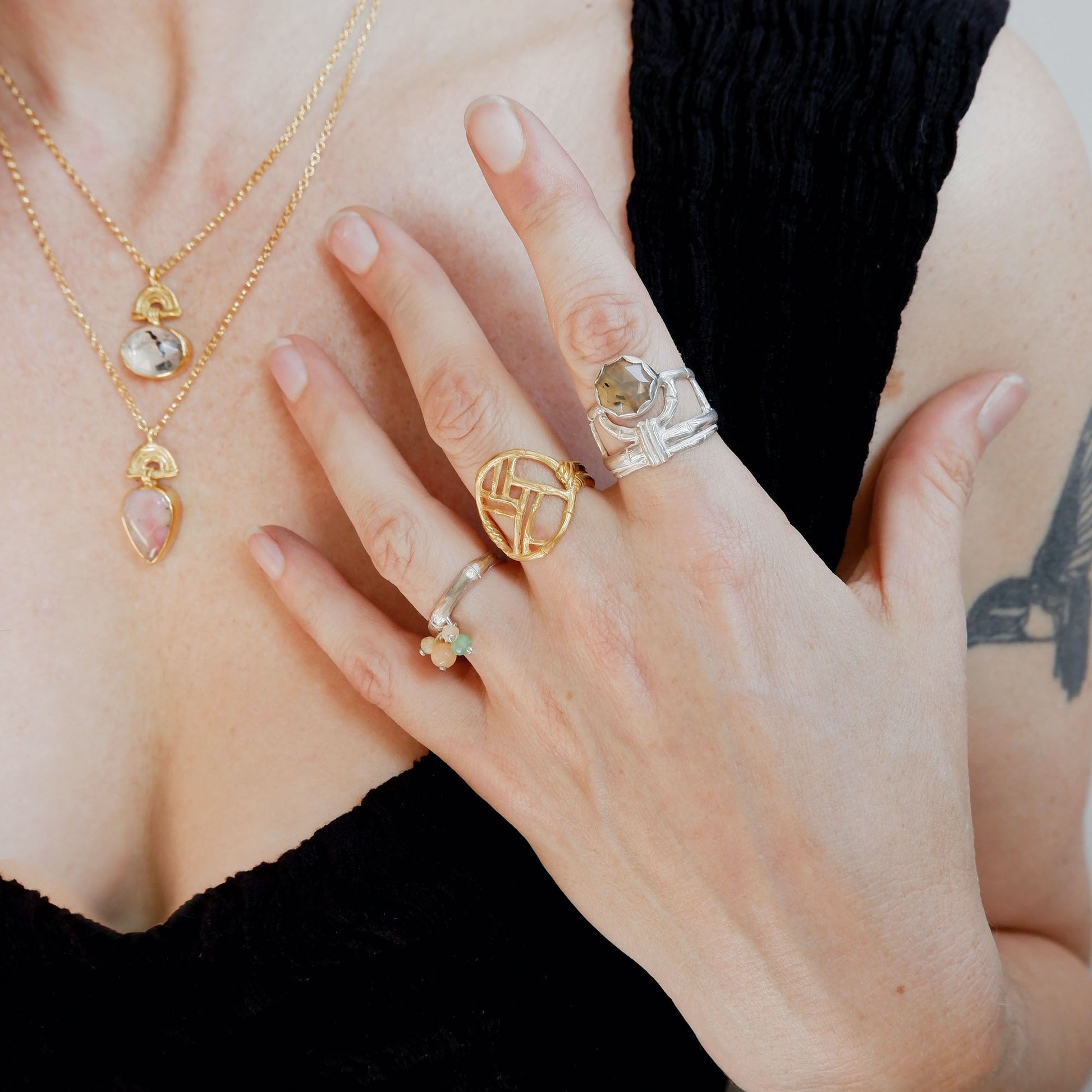 Gold ring with geometric open-work Bamboo Circle screen design, silver open-work bamboo stayle ring with honey coloured Montana Agate gemstone, Sterling silver bamboo band ring, with pastel coloured gemstone beads, on model with two small gold bamboo arch pendants, set with gemstones.