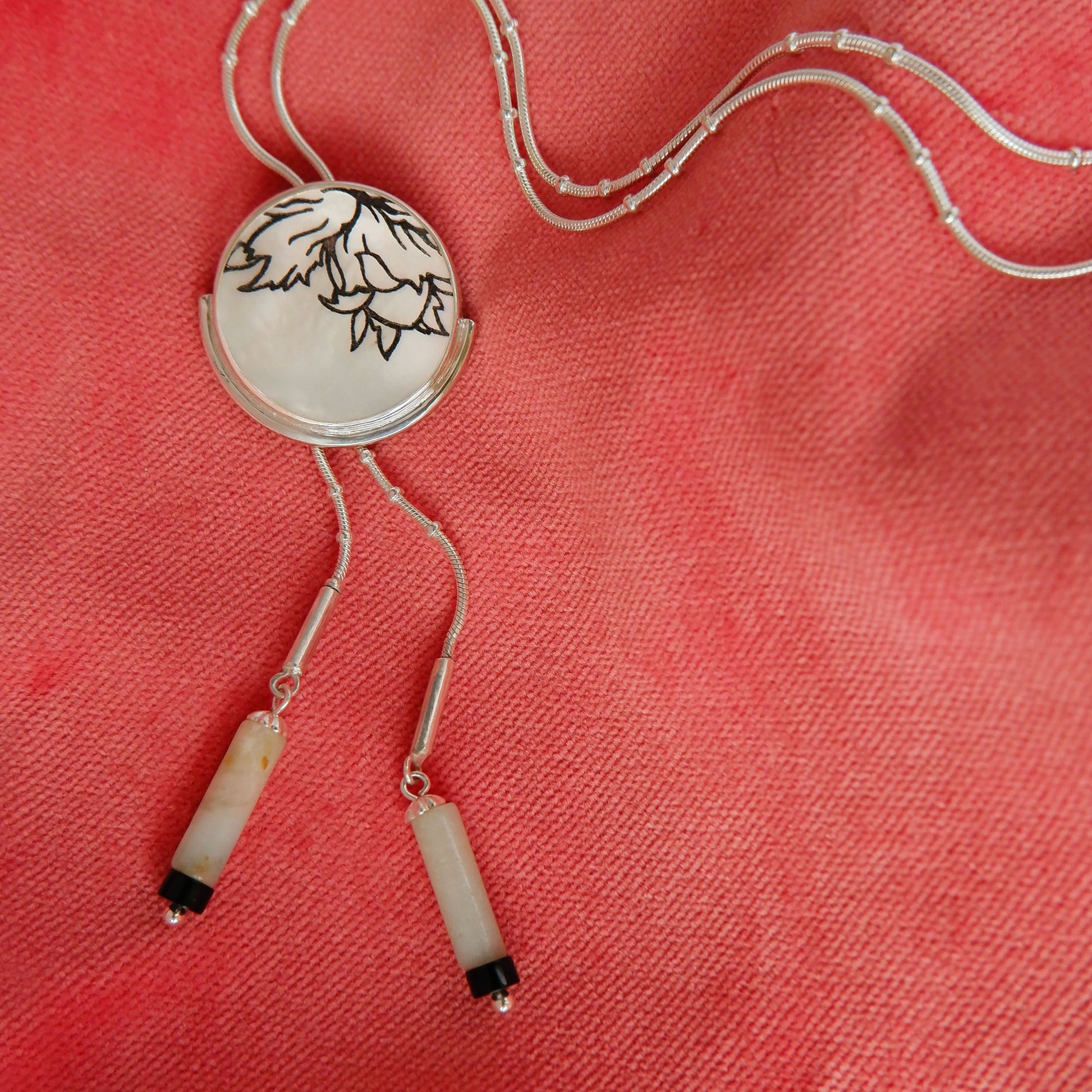 engraved mother of pearl full moon medallion bolo necklet, with sterling silver beaded snake chain and gemstone tips. shown on coral pink velvet.