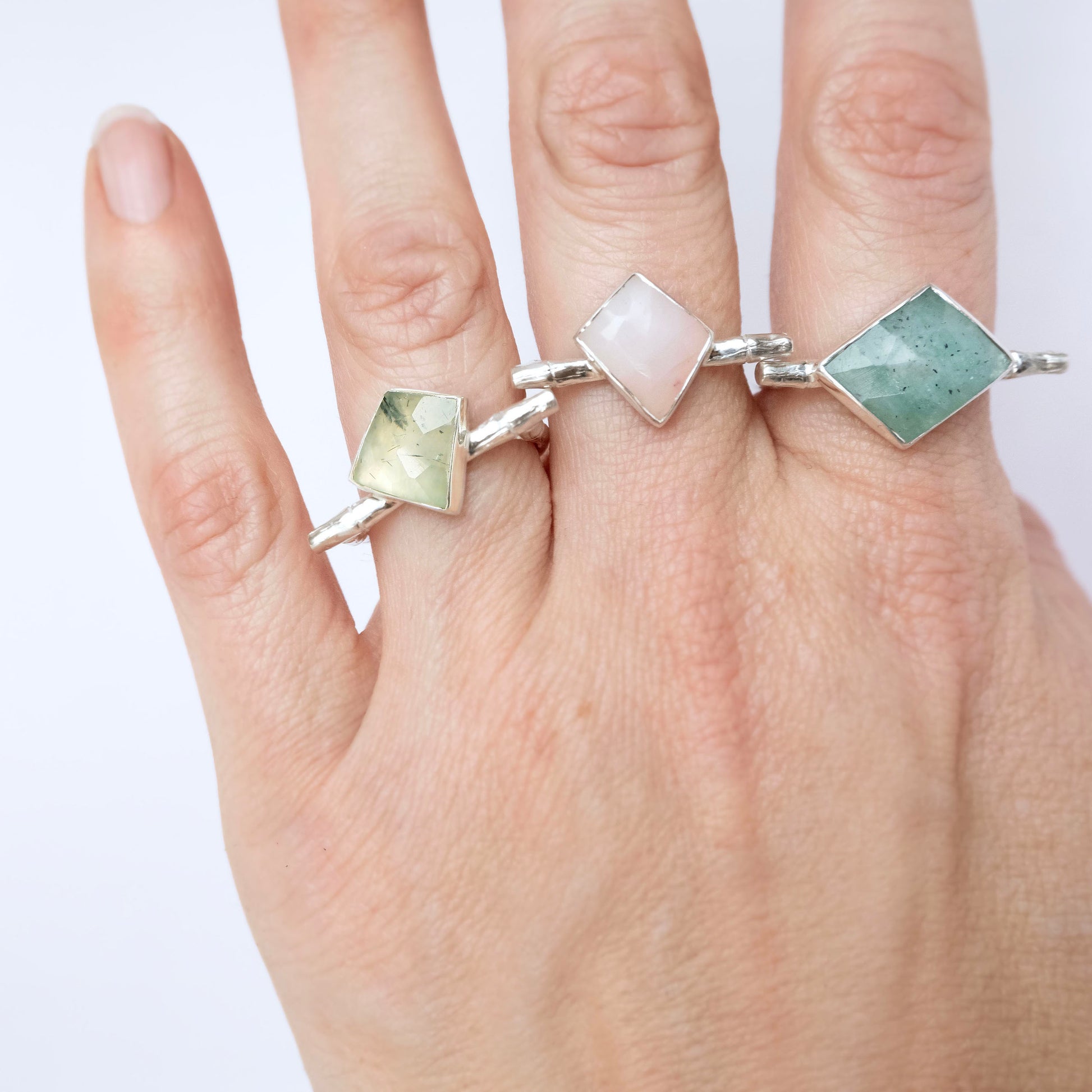 a stack of Sterling Silver and gold vermeil bamboo style rings with irregular angular geometric Chrysoprase gem stones in different shades of green, and pink, on a hand,   against a white background