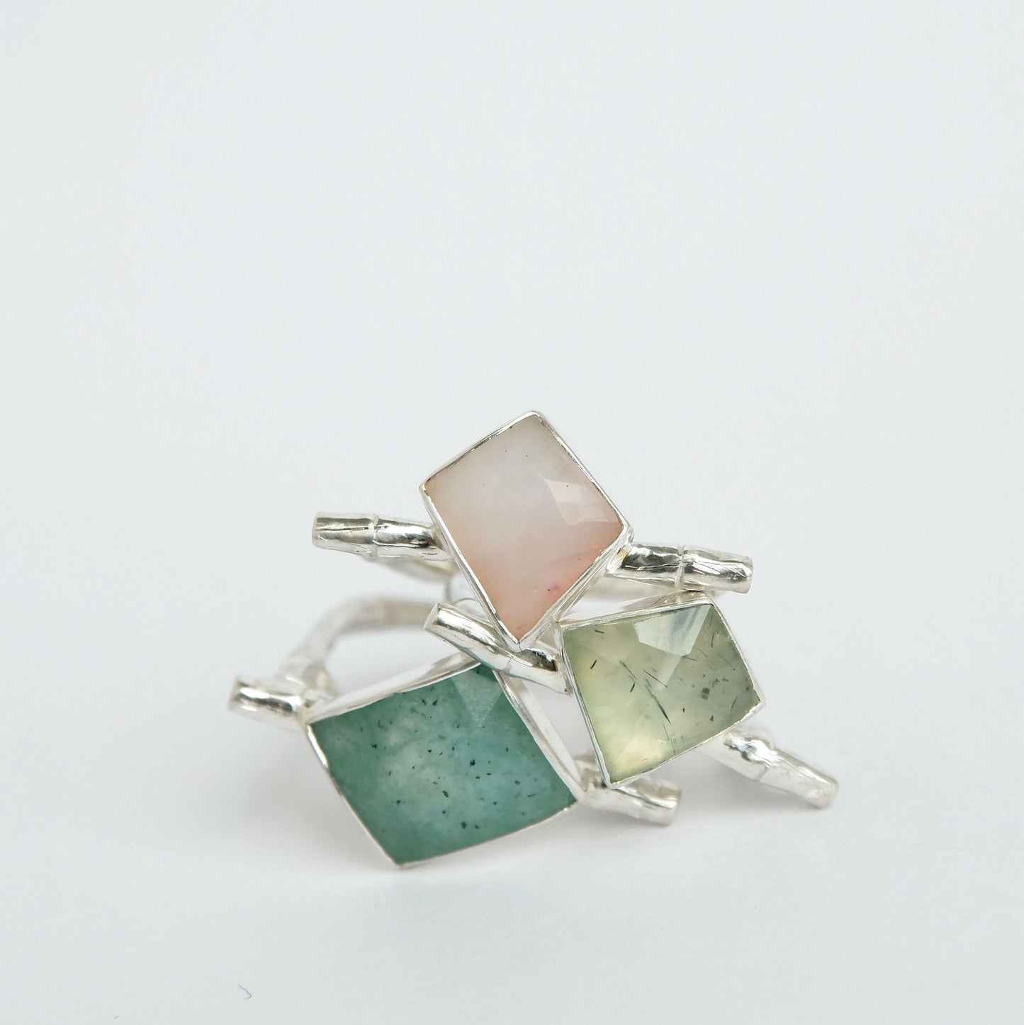 A pile of three Sterling Silver flat top bamboo style ring with a irregular angular geometric Amazonite, pink opal, and Prehnite gem stones, on a white background